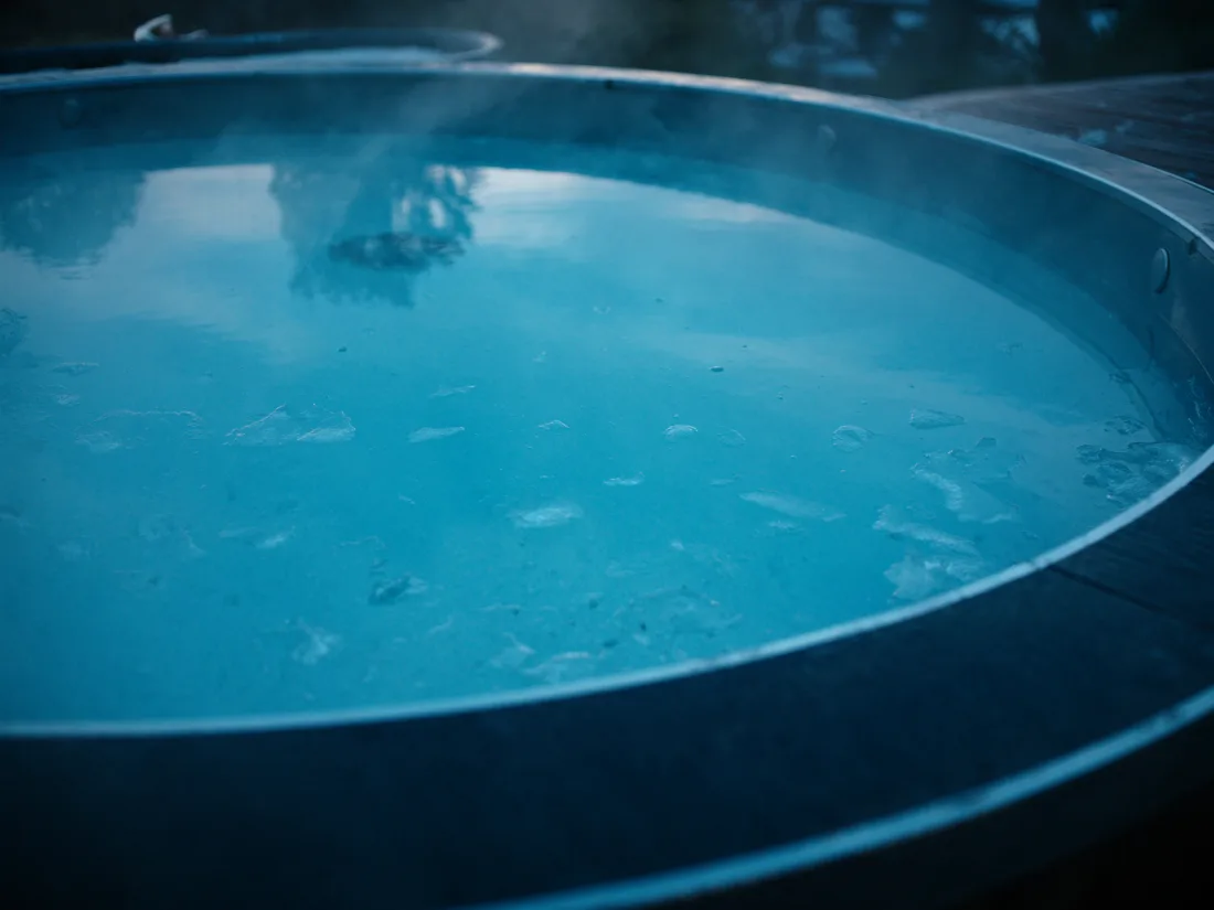 Dark, still cold-plunge water at dawn with vapour lifting off the surface