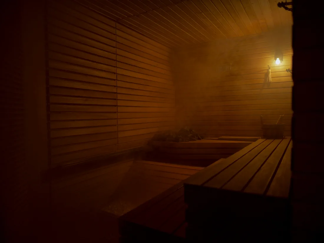 The inside of a cedar sauna lit gold, steam drifting over the timber benches