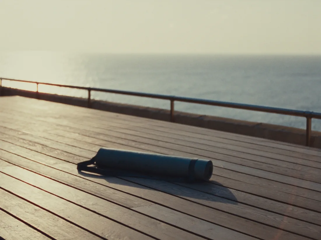 A rolled mat on timber decking above a calm ocean at sunrise